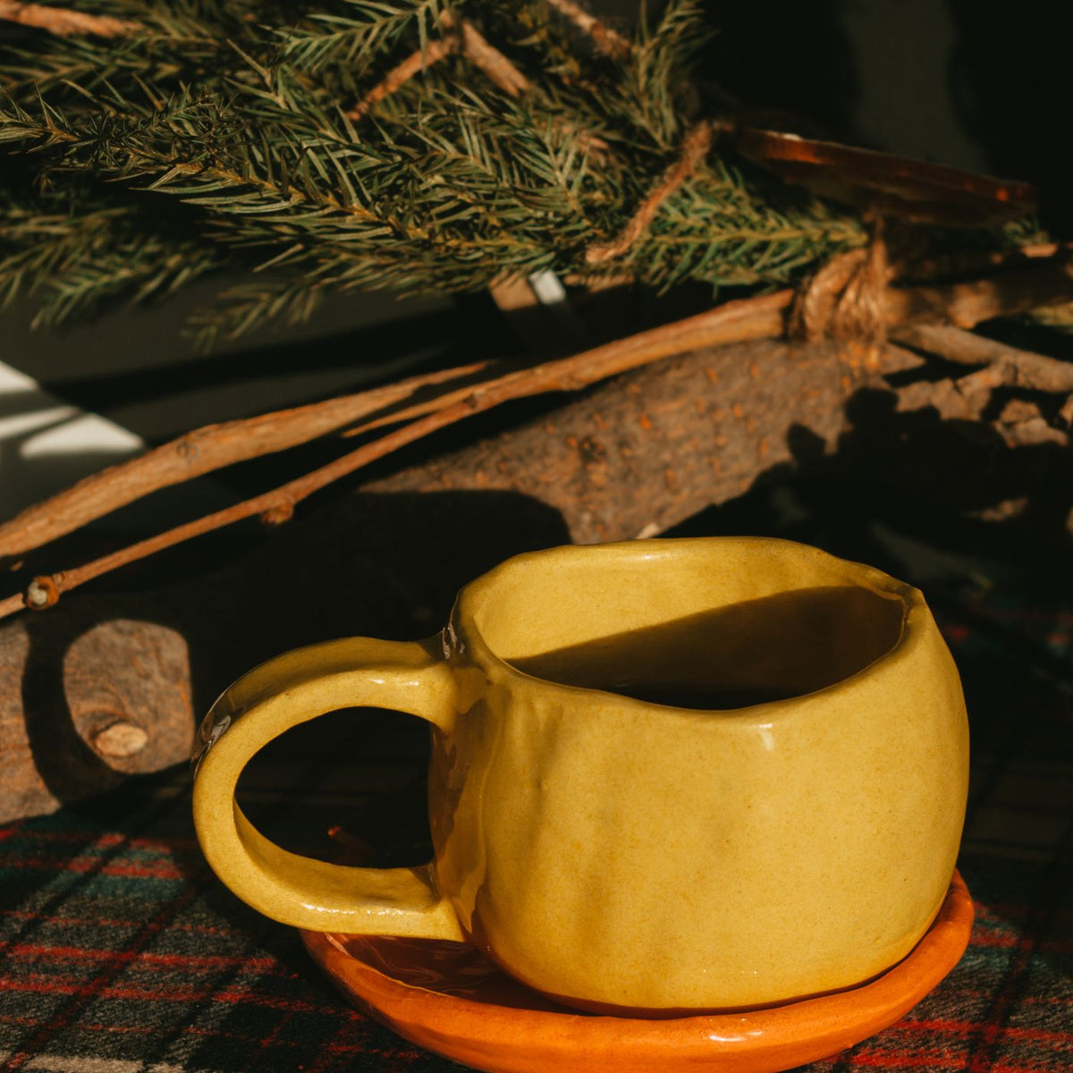 A yellow mug sitting on a plaid tablecloth in warm toned light.
