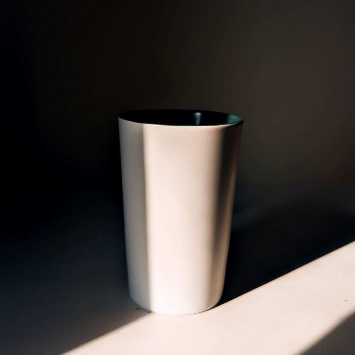 A plain white cup photographed with deep shadows falling across it.