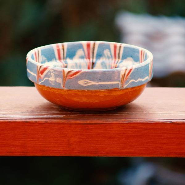 A brightly patterned ceramic bowl photographed outdoors on a wooden table.
