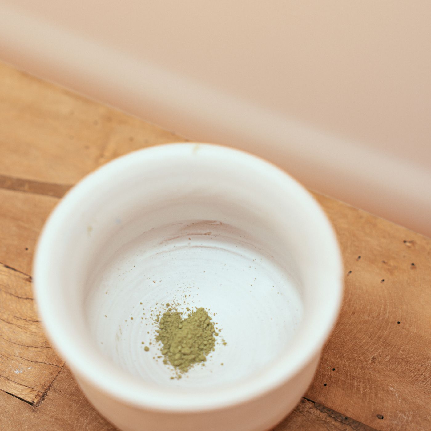 A ceramic bowl holding matcha powder, photographed on a wooden table.